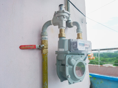 ​Gas meter installation on an outdoor wall, natural gas utility meter with a pressure regulator and a red shut-off valve for residential energy consumption measurement and monitoring