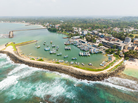 Aerial view of fishing boats moored in a sheltered harbor protected by a stone breakwater along the tropical coastline Hikkaduwa, Southern Province, Sri Lanka.