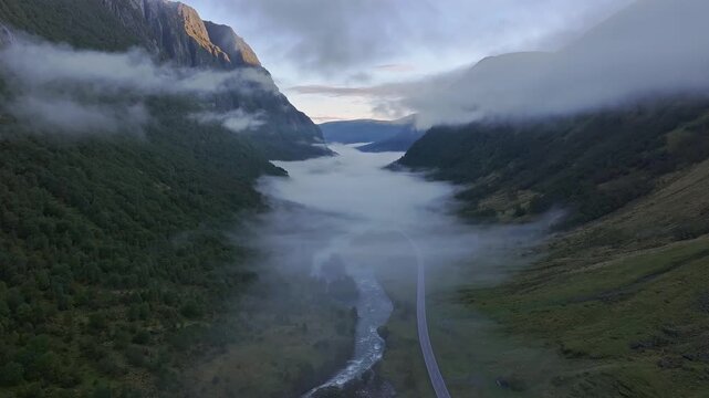 Aerial view of a dramatic Norwegian valley with low clouds, winding river and a road at dawn