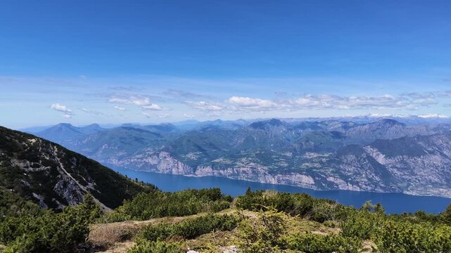 Panoramic view from Monte Baldo overlooking Garda lake with stone cairns, high alpine scenery, dramatic mountain peaks, summer travel destination
