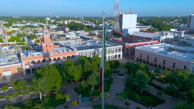 High Aerial View of Municipal Palace and Mexican Flag at Plaza Grande in Merida, Yucatan. Mexico. The composition highlights the elegant, long salmon-pink and white facade of the historic building.