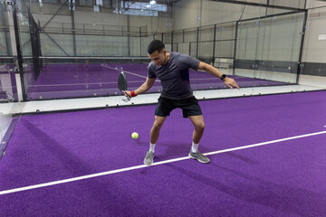 Obraz premium Adult male athlete standing by white line holding paddle hitting yellow ball at purple sports court