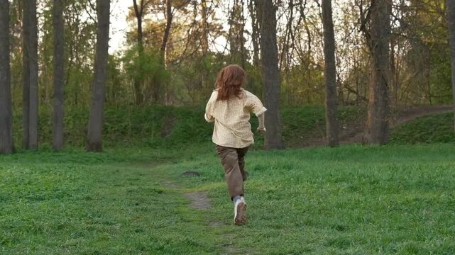 Cinematic &nbsp;summer forest at sunset. Soft warm light. &nbsp;teenage girl with natural red hair and a Scottish appearance runs through a grassy field toward tall trees. Slow-motion footage. Summer holiday 