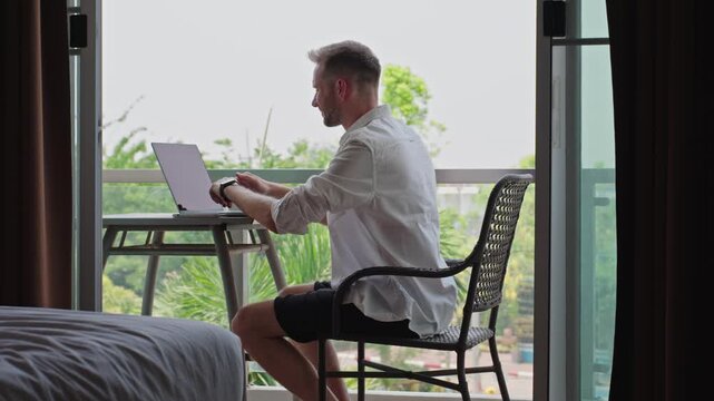 Man Returning To Laptop Work After Smartphone Messaging At Hotel Balcony Workspace, Digital Nomad Workflow And Flexible Remote Business Routine