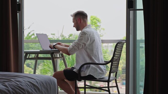 Man Typing On Laptop At Hotel Balcony Workspace During Remote Work Session, Digital Nomad Lifestyle And Flexible Online Business Routine