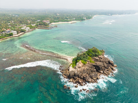 Aerial view of Devil's Rock island surrounded by turquoise ocean waters and lush tropical coastline Ahangama, Southern Province, Sri Lanka.