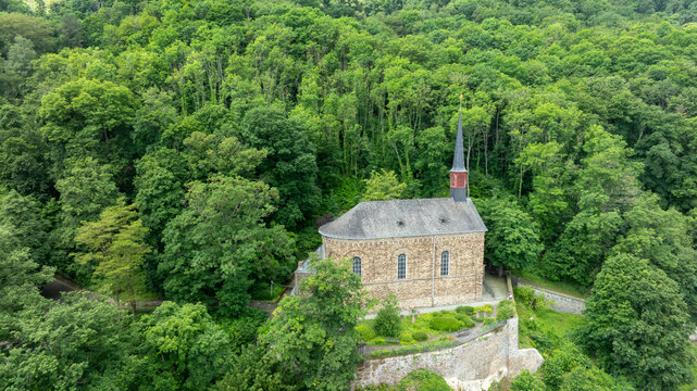 Aerial view of St. Menas church with its stone walls and slender spire surrounded by lush green trees on a hillside in Koblenz, Rheinland-Pfalz, Germany.