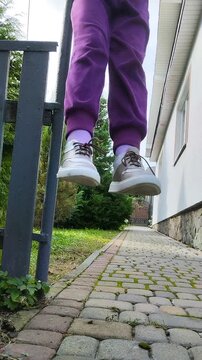 Low angle view of a child jumping or hanging on a playground outdoors, Active kid in purple sweatpants and sneakers playing outside.