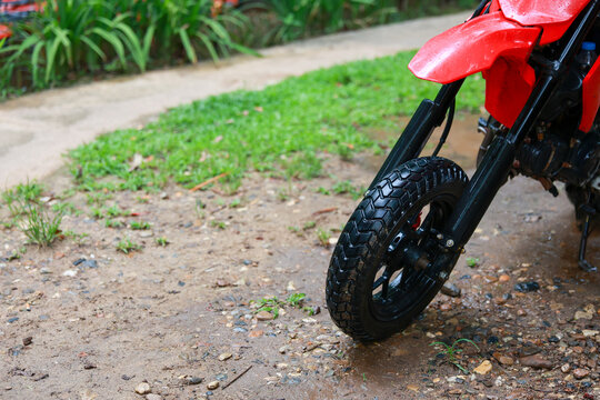 Red toy motorcycle front wheel on wet outdoor path after rain. This nostalgic scene evokes feeling of childhood fun, quiet play, and simple garden recreation
