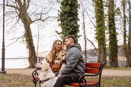 Romantic couple relaxing with golden retriever beside lake in quiet city park