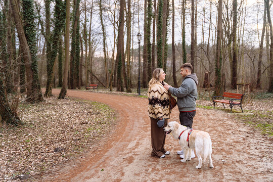 Young couple with dog talking during peaceful forest walk near lakeside park