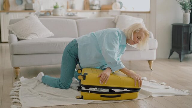 Woman trying to close overfilled suitcase, preparing to summer weekend journey. Overloaded luggage and baggage, senior lady packing things into travel bag, baggage allowance per person, tourist trip