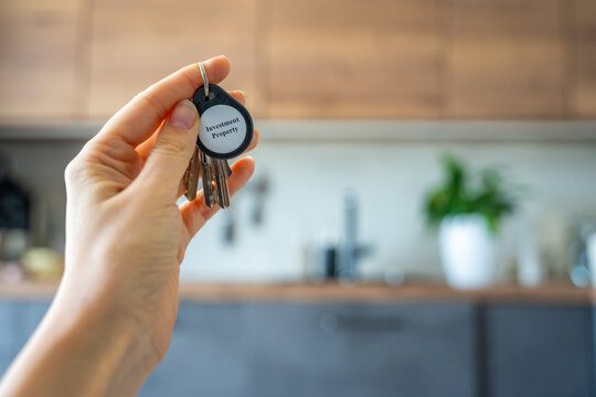 Woman holding house keys with investment property keychain inside modern apartment interior. Real estate investment and property ownership concept for passive income and wealth building