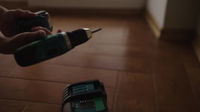 Male worker changing dead battery on cordless electric screwdriver and placing it on charger station to recharge, preparing power tool for home renovation and repair work, close-up, slow motion.