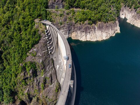 Aerial view of the Verzasca Dam with its massive curved concrete wall nestled between steep rocky cliffs and lush green forests Gordola, Ticino, Switzerland.