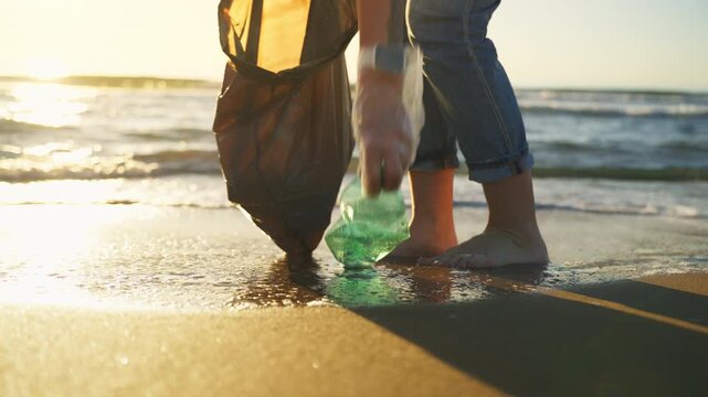 Woman collecting plastic waste from sandy beach with black bag, highlighting ocean pollution problem, marine contamination, and environmental crisis awareness.