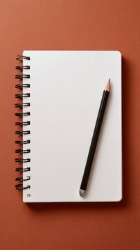 Blank spiral notebook with a black pencil, top view on a solid terracotta colored background. Minimalist stationery for writing notes.