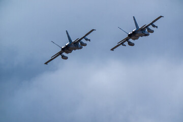 Fototapeta premium Pair of military jet aircraft in synchronized tight formation, both in steep bank with underbellies showing fuel tank and pylon arrays against cloudy sky