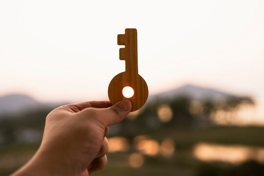 Hand holding wooden key model in sunlight, representing key to success, business goal achievement and career solution concept.