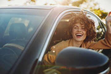 Fototapeta premium A joyful woman in a car with window down, hair in the breeze, bathed in warm retro tones. A candid lifestyle moment that conveys joy, travel, and sunny freedom. Perfect for lifestyle and travel