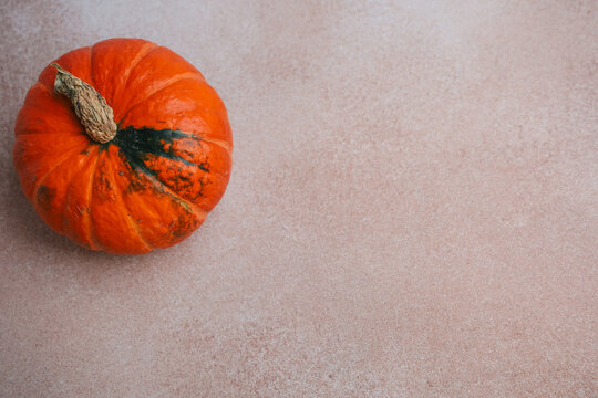 Orange pumpkin sits on a light surface in a simple setting during autumn season to mark the start of harvest celebration