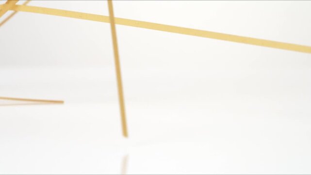 Dry uncooked Linguine Fettucine Bucatini bouncing on a white tabletop in slow motion close up macro before settling.