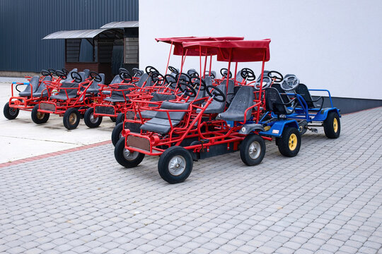 Four-wheeled pedal karts with red roofs parked on stone pavement. Multi-seat surrey bikes for rent, outdoor family entertainment and active leisure activities.