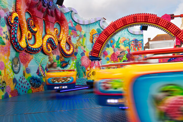 Bright, colorful carnival ride with an octopus mural and spinning cars captured in motion, conveying excitement, energy and family fun at a lively funfair or amusement park under daytime skies. © fotografiemahieu