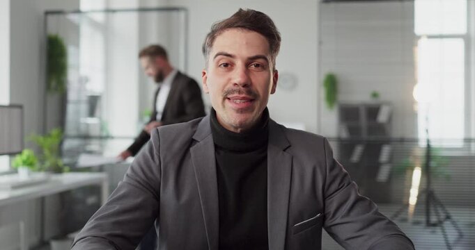 Businessman on webcam in an online video meeting. He greets remote colleagues from a tidy office, discussing progress and sharing updates with a friendly tone. Concept of clear online teamwork.
