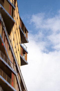 Wood balcony architecture climbs along a warm facade beside sky and cloud, giving an urban building a vertical pattern of shadow and light