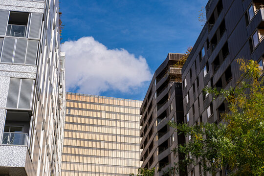 Urban street architecture frames sky and cloud between facade layers, where a building and tree create district depth along the view