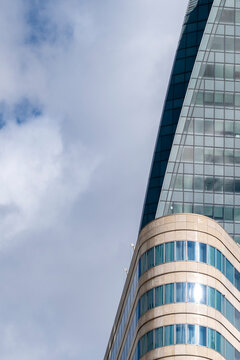 Curved glass tower architecture lifts a reflective facade into sky and cloud, showing urban building lines stacked across a rounded edge