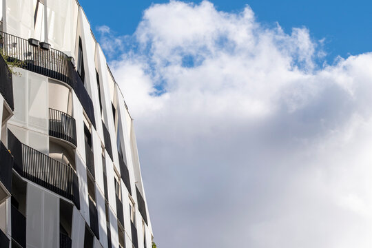 White facade architecture rises with balcony shadows beside sky and cloud, giving an urban building edge a vertical rhythm against light