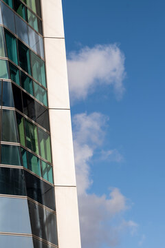 Vertical glass tower architecture frames a reflective facade beside open sky and cloud, showing urban building lines rising along a sharp edge