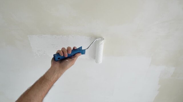 A painter paints the ceiling with white paint using a roller during an apartment renovation. Work in progress