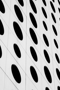 White facade architecture repeats oval windows across an urban building, where black openings and geometric pattern create graphic rhythm