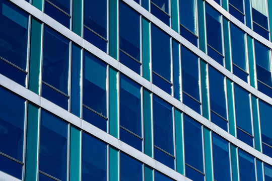 Blue glass facade architecture bends across an urban building, where window grid and reflection create diagonal pattern and depth in daylight
