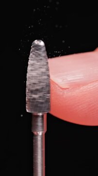 Vertical video. Rotating Professional Manicure Drill Bit Touching Fingernail in Slow Motion, Extreme Macro View of Nail Filing Process With Flying Dust on Black Background