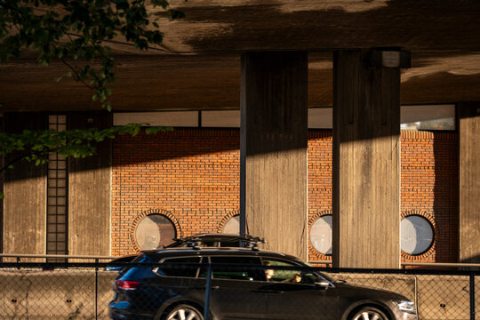 A car moves beneath a concrete bridge in Oslo, where urban infrastructure, brick facade and shadow create layered street depth in daylight