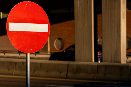 A red restriction sign stands near concrete columns in Oslo, with urban road infrastructure and shadowed traffic beneath a city bridge