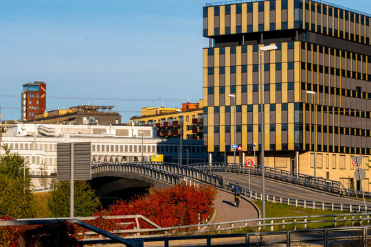 Road infrastructure and a bridge lead through an Oslo urban district, where modern building facade lines and autumn trees open toward the skyline