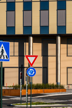 Traffic signs stand before an Oslo building facade, where urban street infrastructure arranges a crosswalk and road edge in daylight