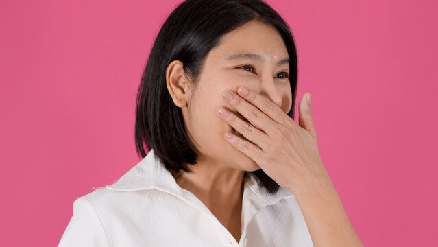 Cheerful Asian Woman Laughing and Covering Her Mouth Against Pink Background