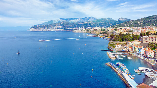 Aerial view of coastal town Sorrento and Gulf of Naples, Italy. Sorrento coastline features colorful buildings overlooking blue Tyrrhenian Sea, with harbor, boats, limestone cliffs, and mountains