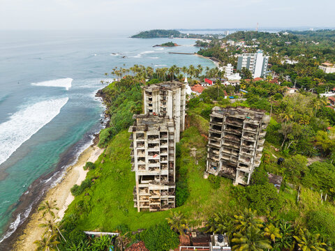Aerial view of abandoned concrete buildings on a lush green cliff overlooking the turquoise ocean and coastline in Mirissa, Southern Province, Sri Lanka.