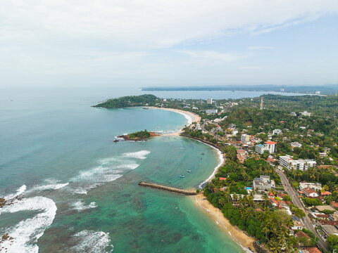 Aerial view of Parrot Rock and the scenic coastline with turquoise ocean waves, sandy beaches, and lush tropical greenery in Mirissa, Southern Province, Sri Lanka.