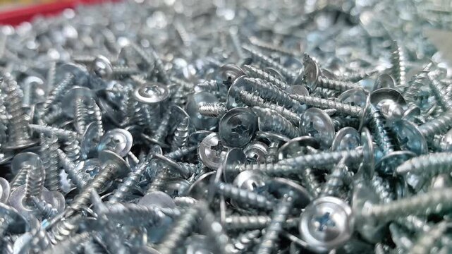 Glimpse a mesmerizing collection of shiny silver screws nestled together in a bustling factory. Each screw glistens under bright lights, showcasing their detailed craftsmanship.
