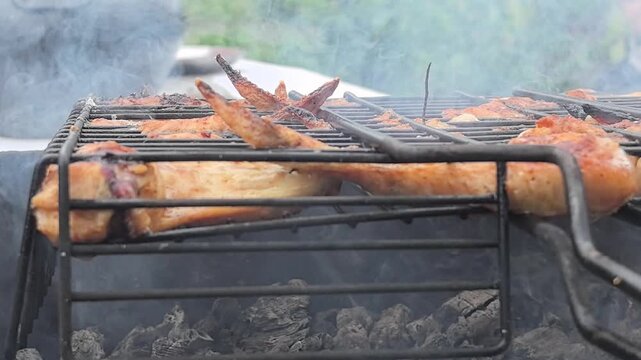 Juicy chicken wings sizzle over an open flame, enveloped in fragrant smoke. The sun casts warm light as the cook expertly flips and seasons for delicious flavors.