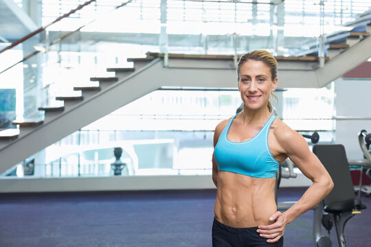 Fit female standing in modern gym near metal glass staircase wearing teal sports bra, copy space