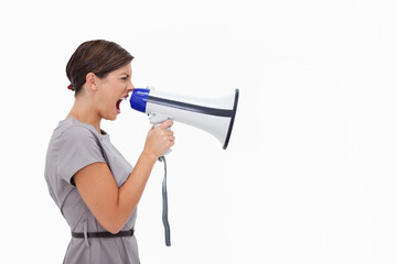 Woman shouting into megaphone, standing by white backdrop in gray dress, thin dark belt, hair clip © wavebreak3